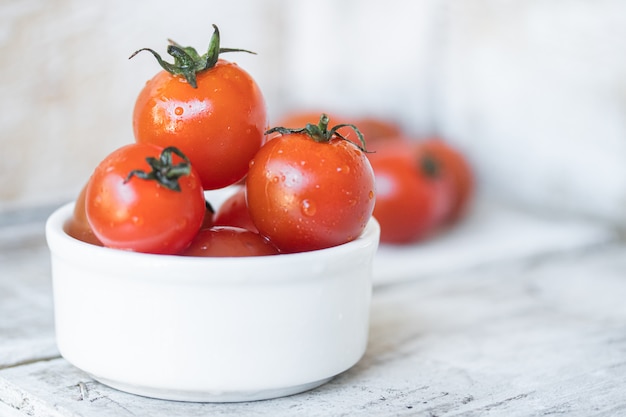 Cherry tomatoes in white ceramic bowl on white wood