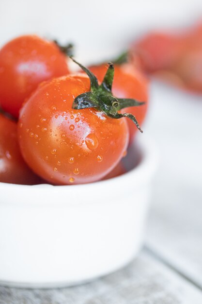 Cherry tomatoes in white ceramic bowl on white wood