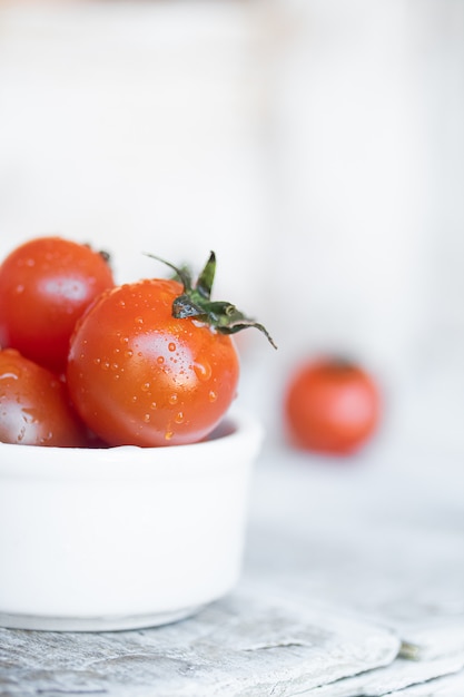 Cherry tomatoes in white ceramic bowl on white wood