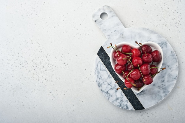 Cherry with water drops on heart shaped plate on white stone table. Fresh ripe cherries. Sweet red cherries. Top view. Rustic style. Fruit Background