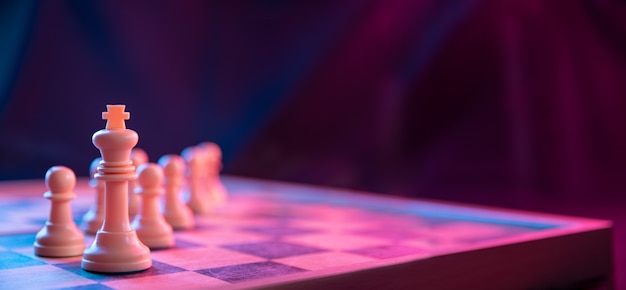 Chess pieces on a chessboard on a dark surface shot in neon pink-blue colors .Close up.