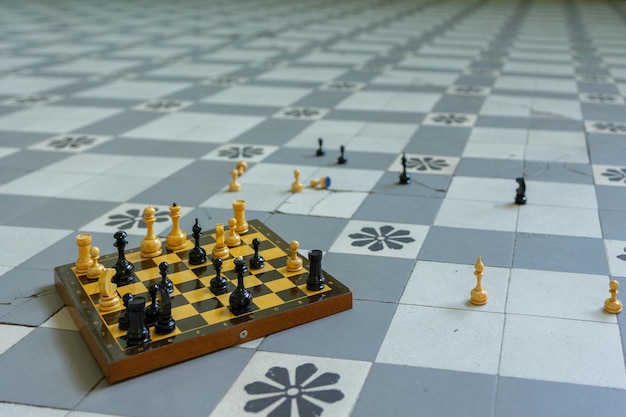 Chessboard with scattered figures stands on checkered floor