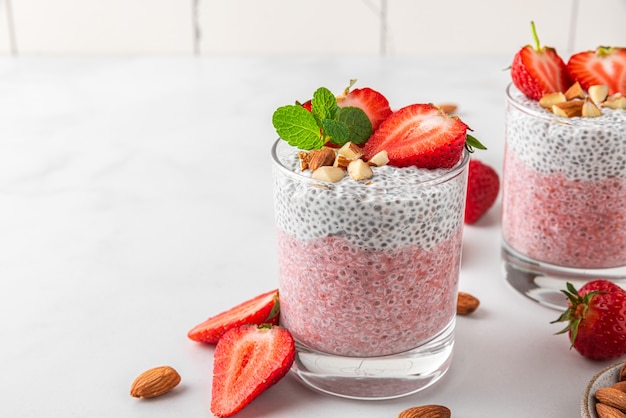 Chia pudding in glasses with fresh strawberries, almonds and mint on white surface for vegan breakfast