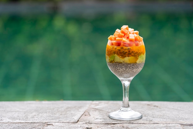 Chia seeds pudding with papaya passion fruit mango and avocado in a glass for breakfast on the background of the swimming pool water closeup The concept of healthy eating superfood