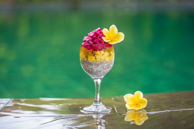 Chia seeds pudding with red dragon fruit, passion fruit, mango and avocado in a glass for breakfast on the background of the swimming pool water, close up. The concept of healthy eating.