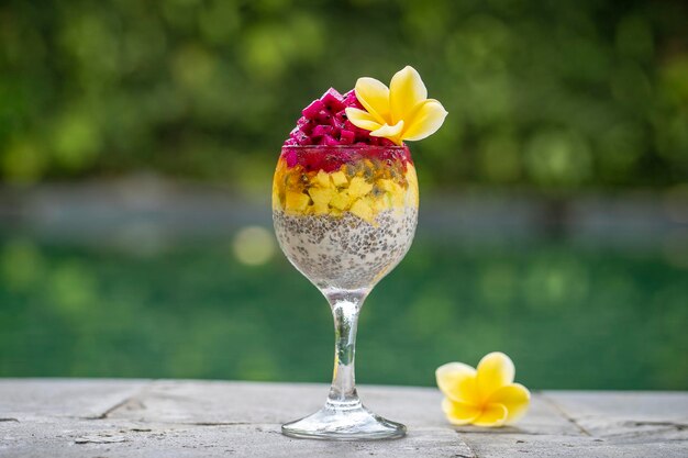 Chia seeds pudding with red dragon fruit passion fruit mango and avocado in a glass for breakfast on the background of the swimming pool water close up The concept of healthy eating