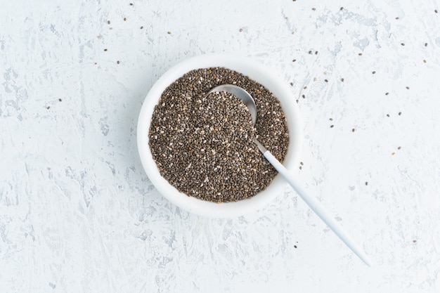 Chia seeds in white bowl on white stone concrete , top view,