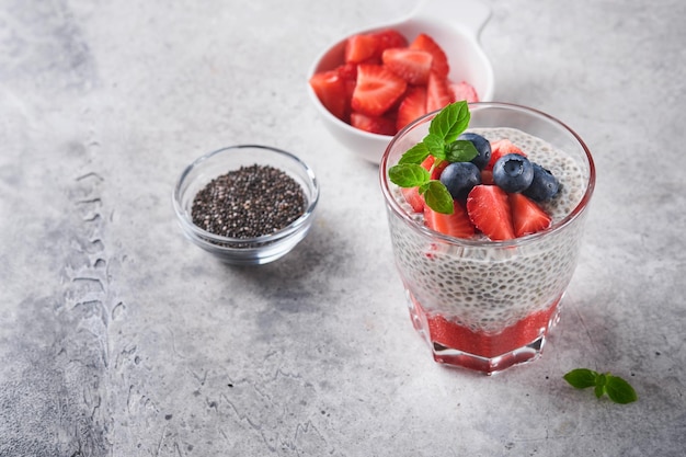 Chia strawberry pudding Healthy vegan breakfast chia seeds pudding with fresh berries and mint in glass on gray concrete background Concept of healthy eating dieting fitness menu Selective focus