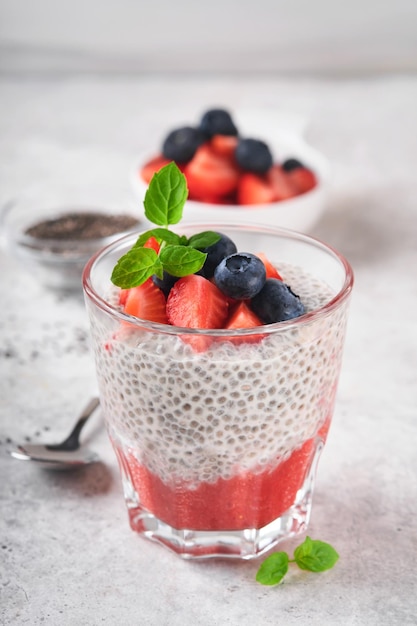 Chia strawberry pudding Healthy vegan breakfast chia seeds pudding with fresh berries and mint in glass on gray concrete background Concept of healthy eating dieting fitness menu Selective focus