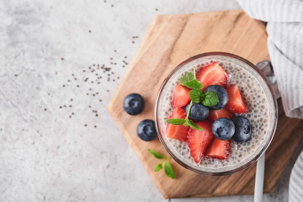 Chia strawberry pudding Healthy vegan breakfast chia seeds pudding with fresh berries and mint in glass on gray concrete background Concept of healthy eating dieting fitness menu Selective focus