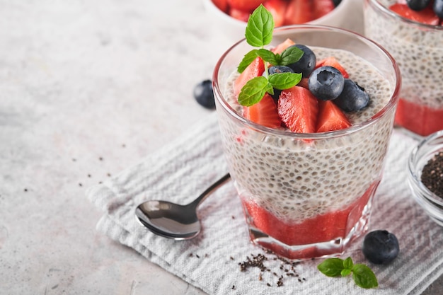 Chia strawberry pudding Healthy vegan breakfast chia seeds pudding with fresh berries and mint in glass on gray concrete background Concept of healthy eating dieting fitness menu Selective focus