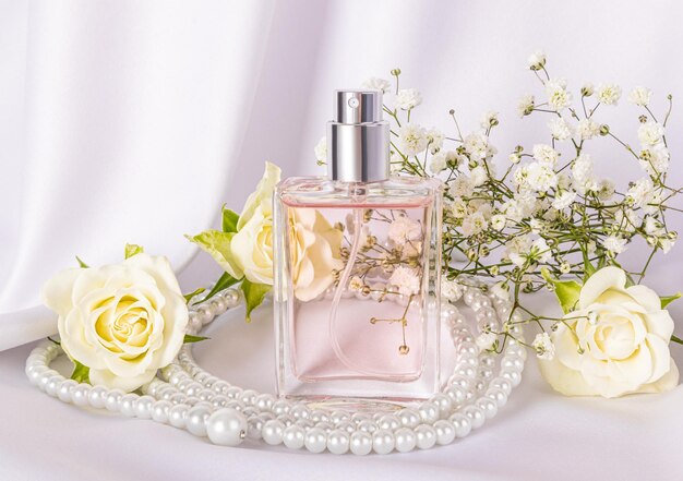 A chic bottle of womens perfume with a floral delicate fragrance on a white satin background with pearl beads Front view Product presentation