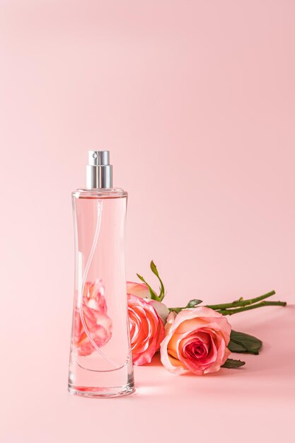 A chic tall bottle of womens perfume on a pastel background with a three tea rose Vertical view Presentation of the delicate fragrance of perfume