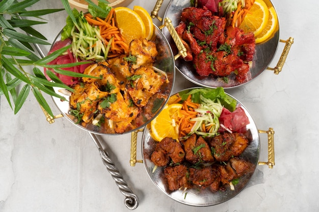 Chicken, beef, and pork shashlik with vegetable garnish and spicy spices, cooked in tandoor. A set of three hot meat dishes in traditional Indian plates.