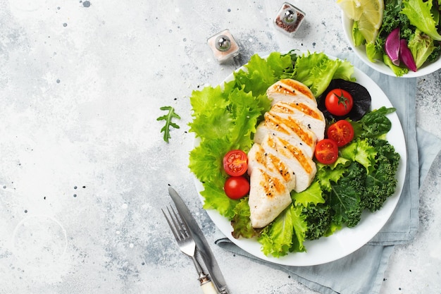 Chicken breast fillet and vegetable salad with tomatoes and green leaves on a light background The concept of healthy food and keto diet Top view with copy space