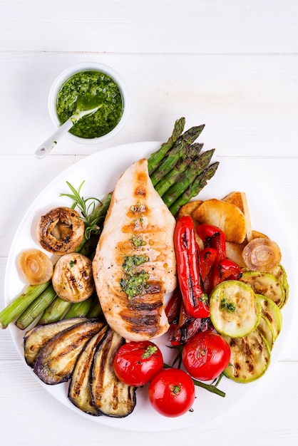 Chicken breast grill with bbq vegetables and pesto sauce in a plate on wood