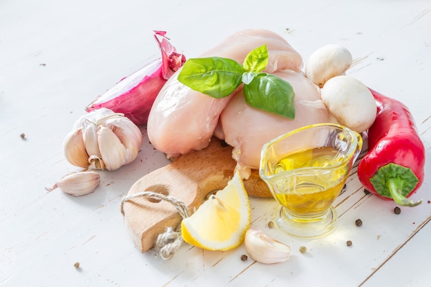 Chicken breast and ingredients on white wood background