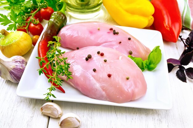 Chicken breast raw in plate with vegetables on light board