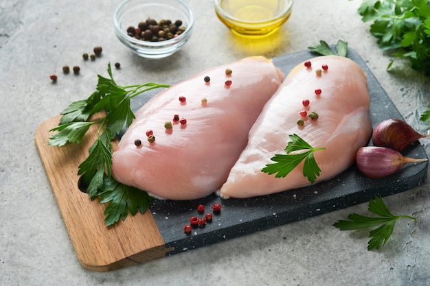 Chicken breast Two Chicken fillet with spices olive oil and parsley on black stone cutting board on grey stone table background Top view with copy space Food meat cooking background