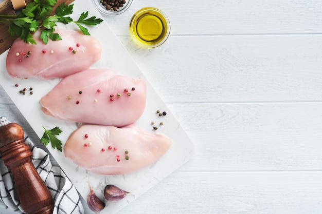 Chicken breast Two Chicken fillet with spices olive oil and parsley on white stone cutting board on white wooden table background Top view with copy space Food meat cooking background