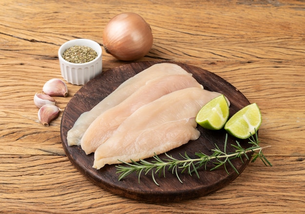 Chicken breast over wooden board with seasonings.