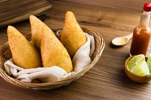 Chicken Coxinha known as Coxinha in Brazil Served in the basket with spices such as lemon and pepper on the side Wooden table in the background Traditional brazilian snack Selective focus