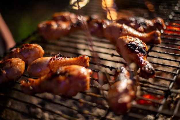 Chicken drumsticks are grilled on a barbecue grill in the evening