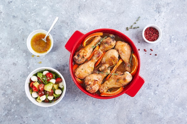 Chicken drumsticks with oranges and thyme baked in red round baking dish