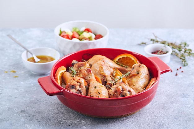 Chicken drumsticks with oranges and thyme baked in red round baking dish