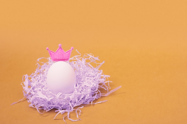 Chicken Easter egg with a pink crown lies in a nest of shredded paper. Space for text