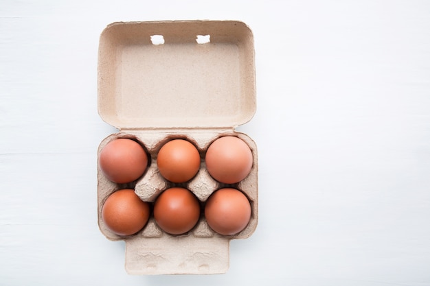 Chicken eggs in egg box on white wooden background