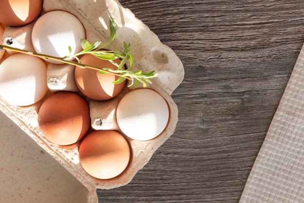 Chicken eggs and a loose sprig of willow are in a cardboard box on a gray wooden table