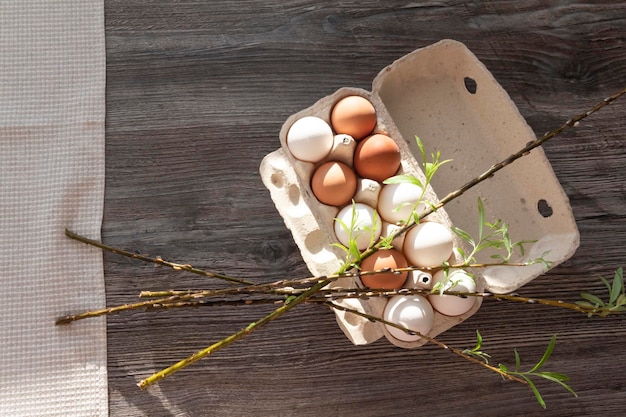 Chicken eggs and a loose sprig of willow are in a cardboard box on a gray wooden table