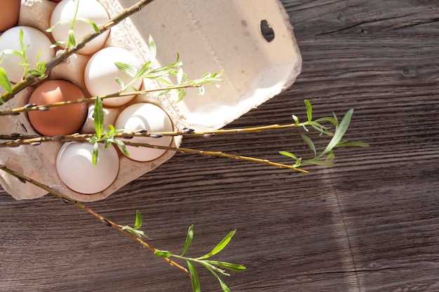 Chicken eggs and a loose sprig of willow are in a cardboard box on a gray wooden table