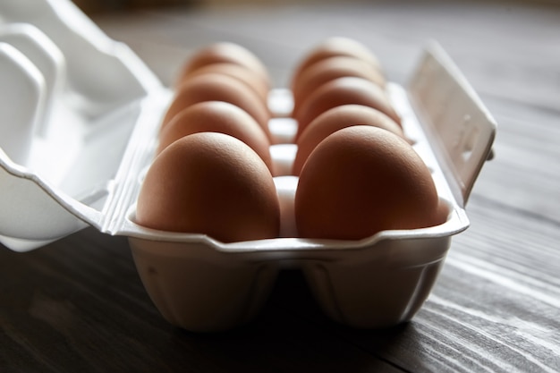 Chicken eggs in a white container on a brown wooden table