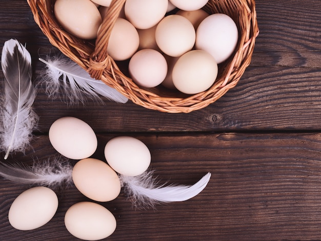 Chicken eggs in a wicker basket on a wooden brown table, top view