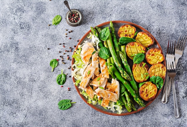 Chicken fillet cooked on a grill with a garnish of asparagus and baked potatoes. Top view