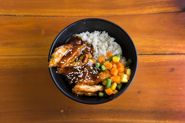 Chicken katsu rice bowl with vegetables and corn on wooden background