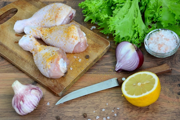 chicken legs with spices on cutting board isolated with green salad, onion, garlic and lemon