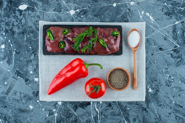 Chicken livers on a board next to vegetables and spices on the towel on the blue surface