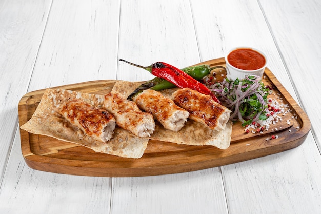 Chicken lula kebabs with grilled vegetables and red sauce on wooden desk