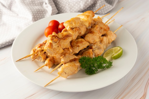 Chicken meat on bamboo skewers kebab in white plate, marble bright background. Diet low fat food.