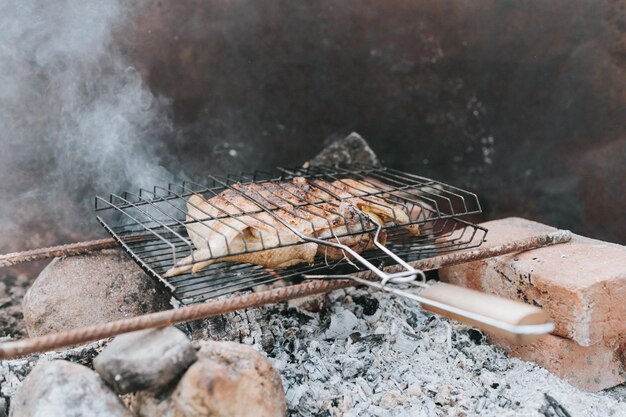 Chicken meat food are fried on grill on smoldering coals or ember from a campfire on the ground on summer or autumn day barbecue in camping conditions survival on countryside and wild rustic life