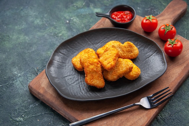 Chicken nuggets on a black plate and fork on wooden board tomatoes ketchup on dark surface with free space close up shot