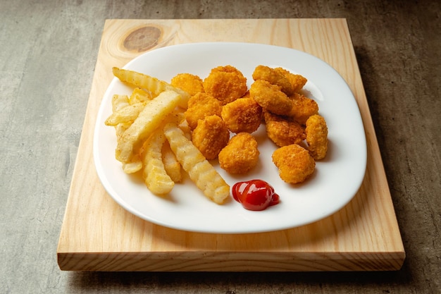 Chicken nuggets and french fries with a little tomato sauce on a plate on a wooden surface ready to eat quick meal