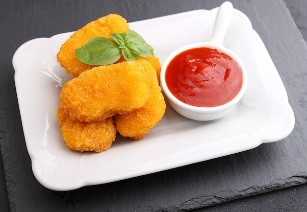 Chicken nuggets with tomato sauce decorated with basil in a white plate