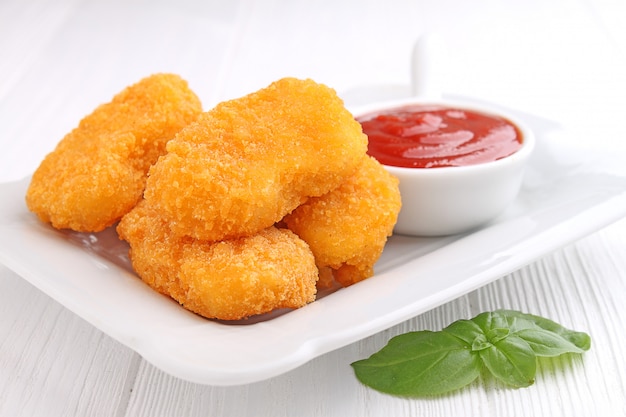 Chicken nuggets with tomato sauce decorated with basil in a white plate