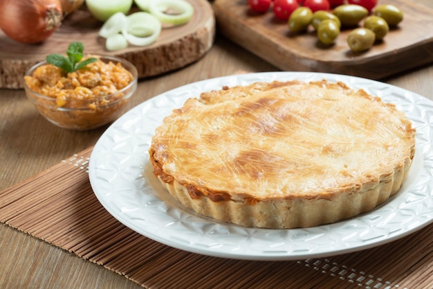 Chicken pie with cottage cheese tomatoes onion and olives on wooden table and white plate