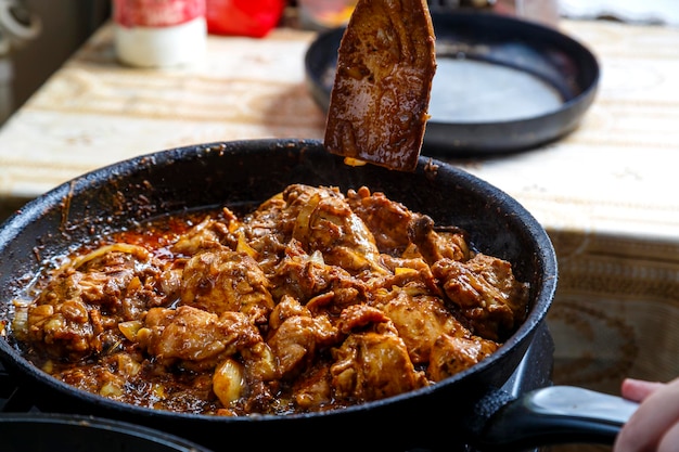 Chicken pieces fried in sauce in spices in a deep frying pan with a wooden spatula