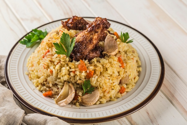 Chicken pilaf in a light plate with baked garlic and fresh herbs on a white wooden background. A traditional eastern dish. Side view. Horizontal orientation with a copy space for the text.